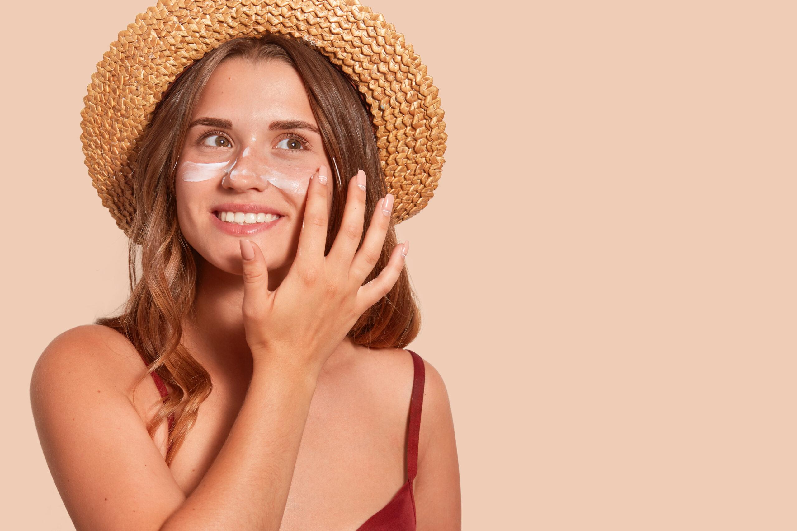 Woman in sunhat applying sunscreen to her cheeks.